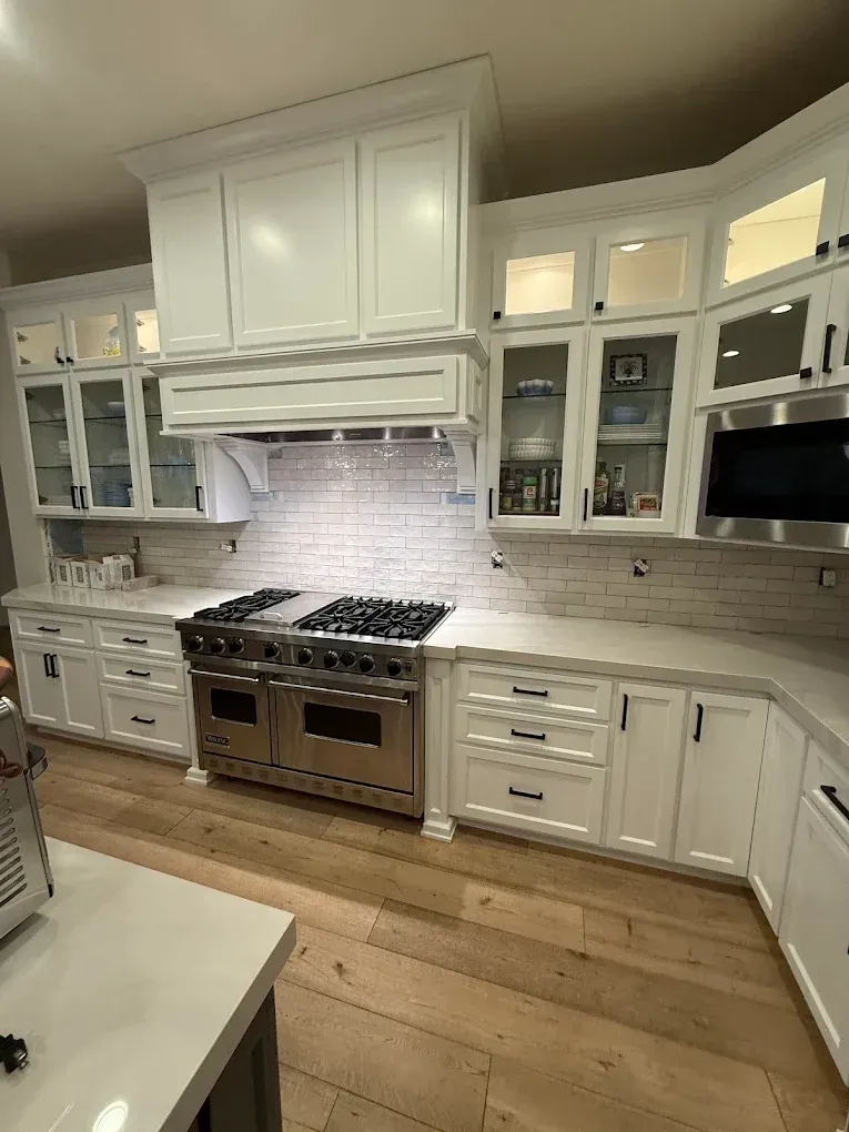 White kitchen with stainless steel oven, white cabinets, brick backsplash, and hardwood floors.
