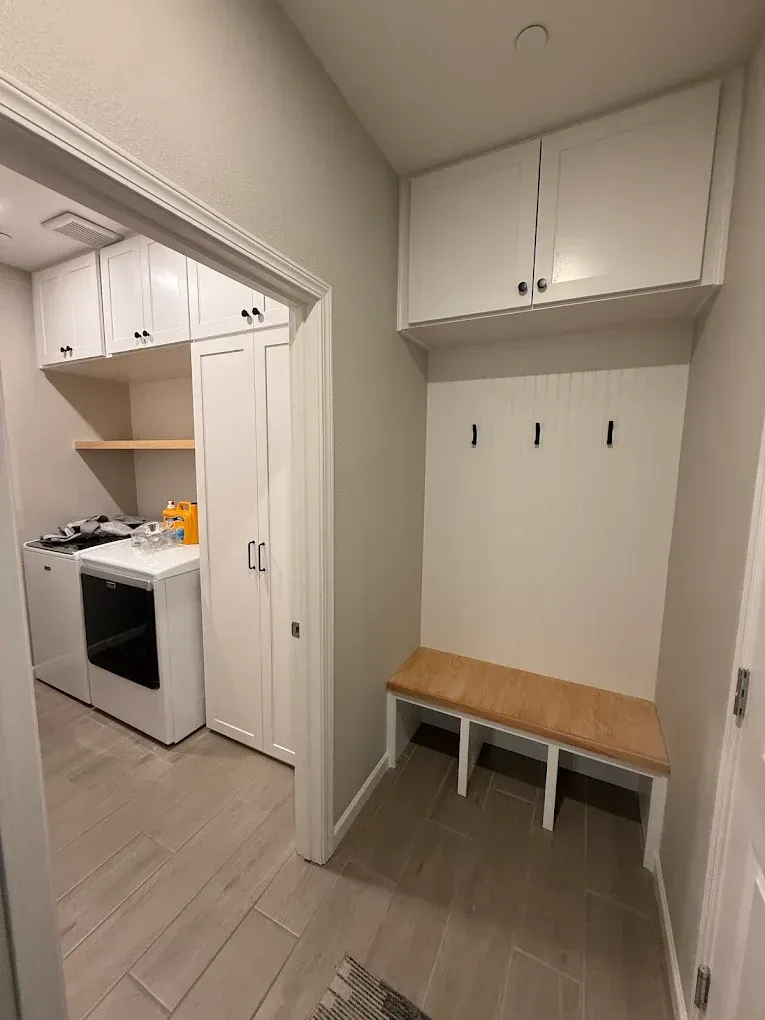 Laundry room with white cabinets, a bench with hooks, and open doorway to washing machine.