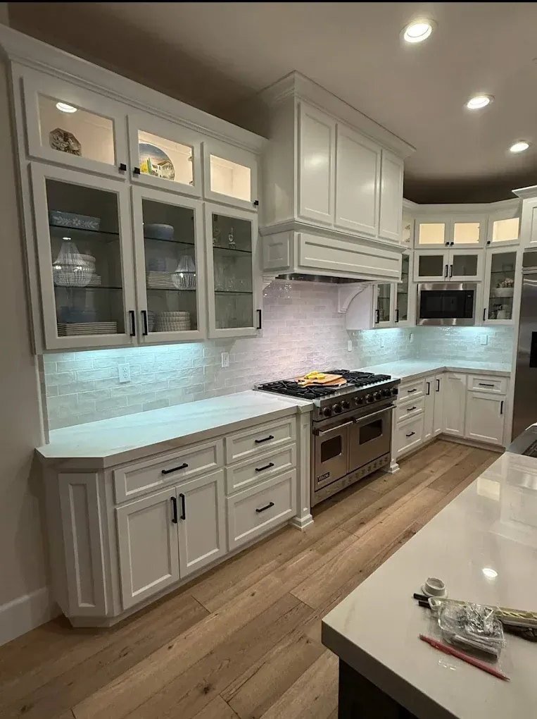 White kitchen with cabinets, marble backsplash, stainless steel range, and wood flooring.