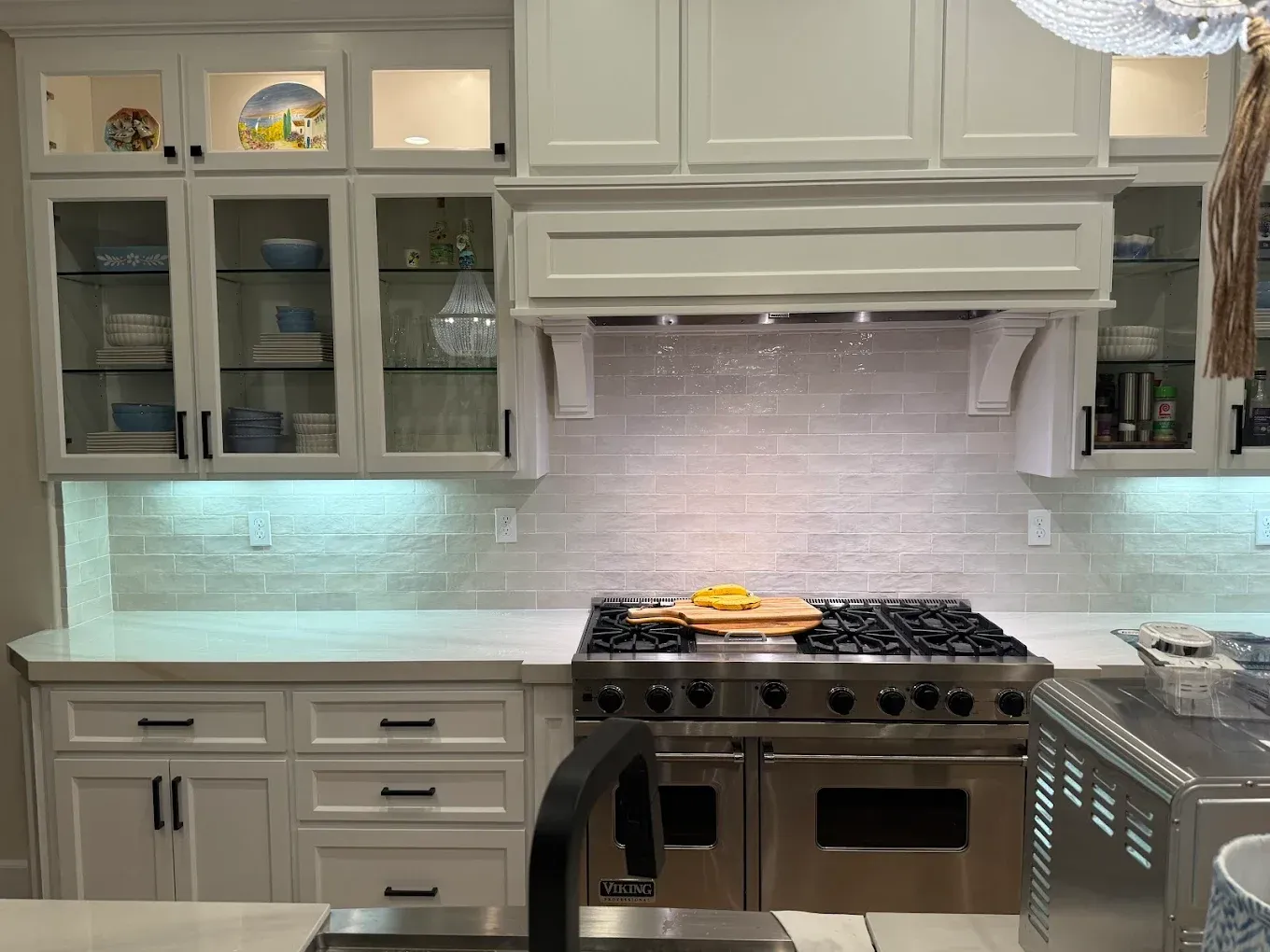 White kitchen with stainless steel oven, cabinets, and light blue tile backsplash.