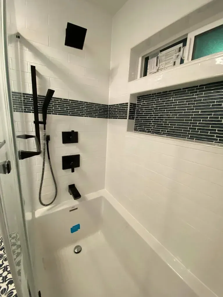 Modern white bathroom with black fixtures; bathtub with a glass shower door.
