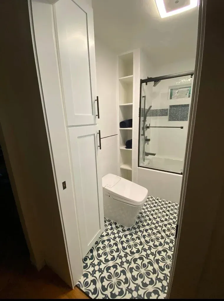 White bathroom with patterned floor tiles, tall storage cabinets, and a glass shower door.