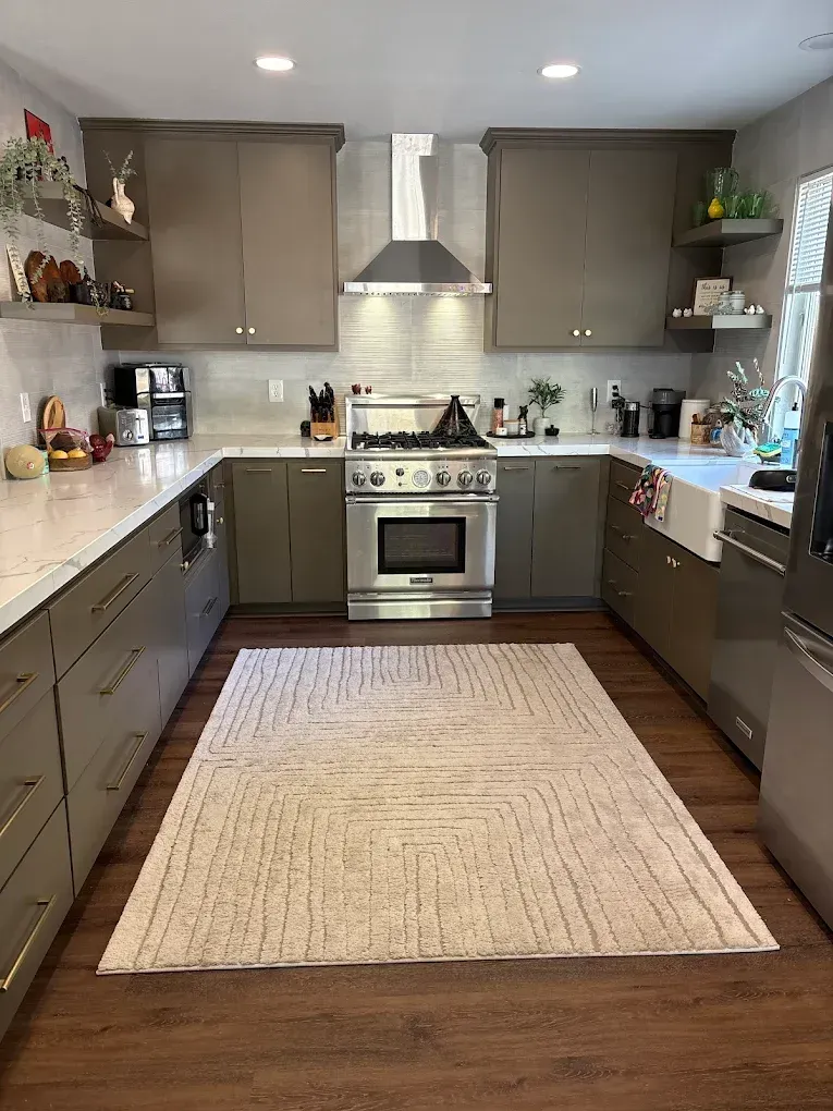 Kitchen with gray cabinets, white countertops, stainless steel appliances, and a patterned rug on a wood floor.
