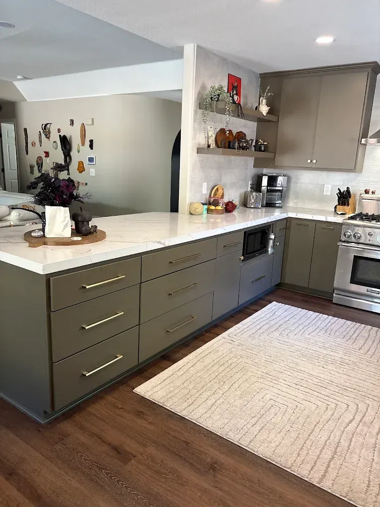 Modern kitchen with olive green cabinets, white countertops, and stainless steel appliances.