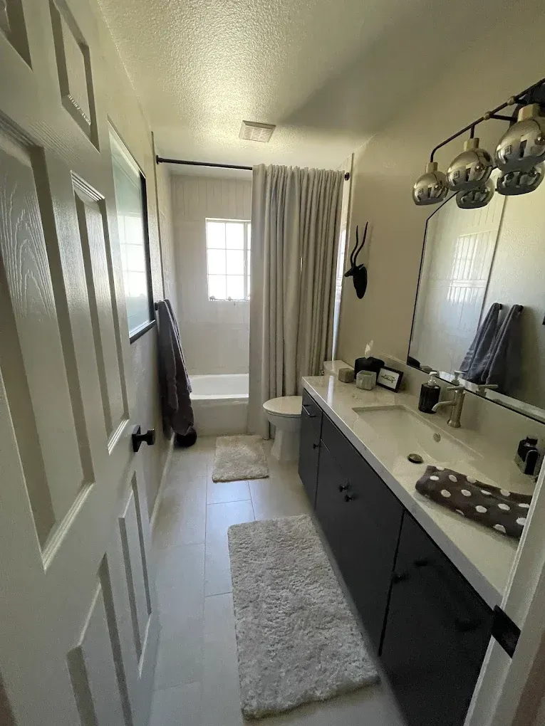 Bathroom with white walls, dark cabinets, a long vanity, and a tub/shower area.