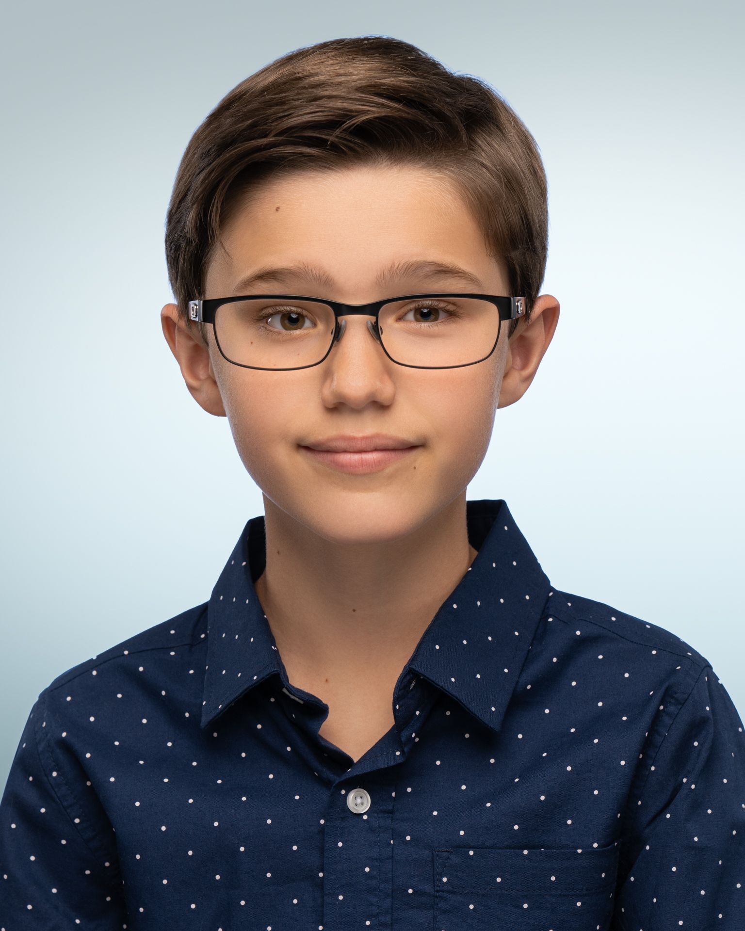 Person wearing a bright blue polo shirt with a buttoned collar, posed against a smooth dark gray background. The hair is neatly styled, and the lighting is soft and even, creating a professional studio portrait look.