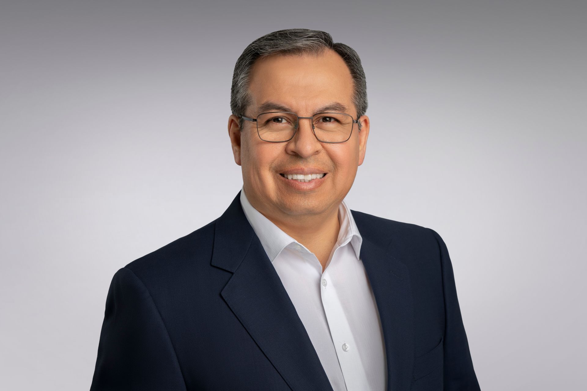 Professional business headshot of executive wearing glasses and blazer on white studio background