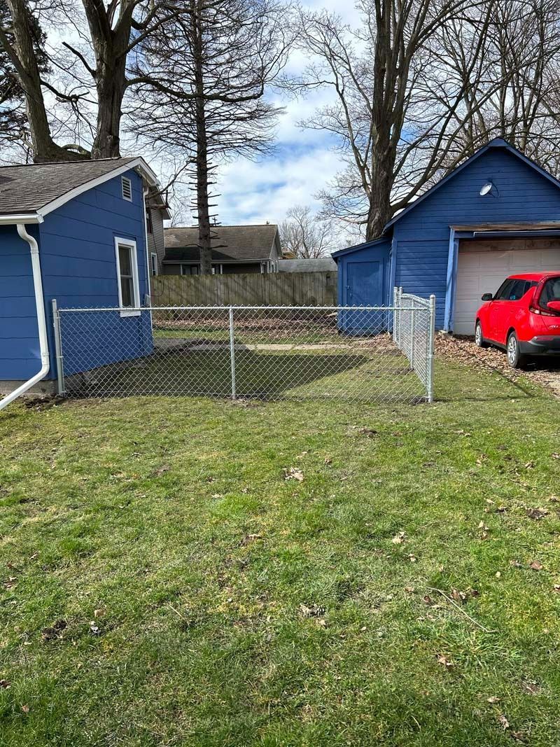 Backyard with blue garages, chain link fence, red truck, trees, and grass.
