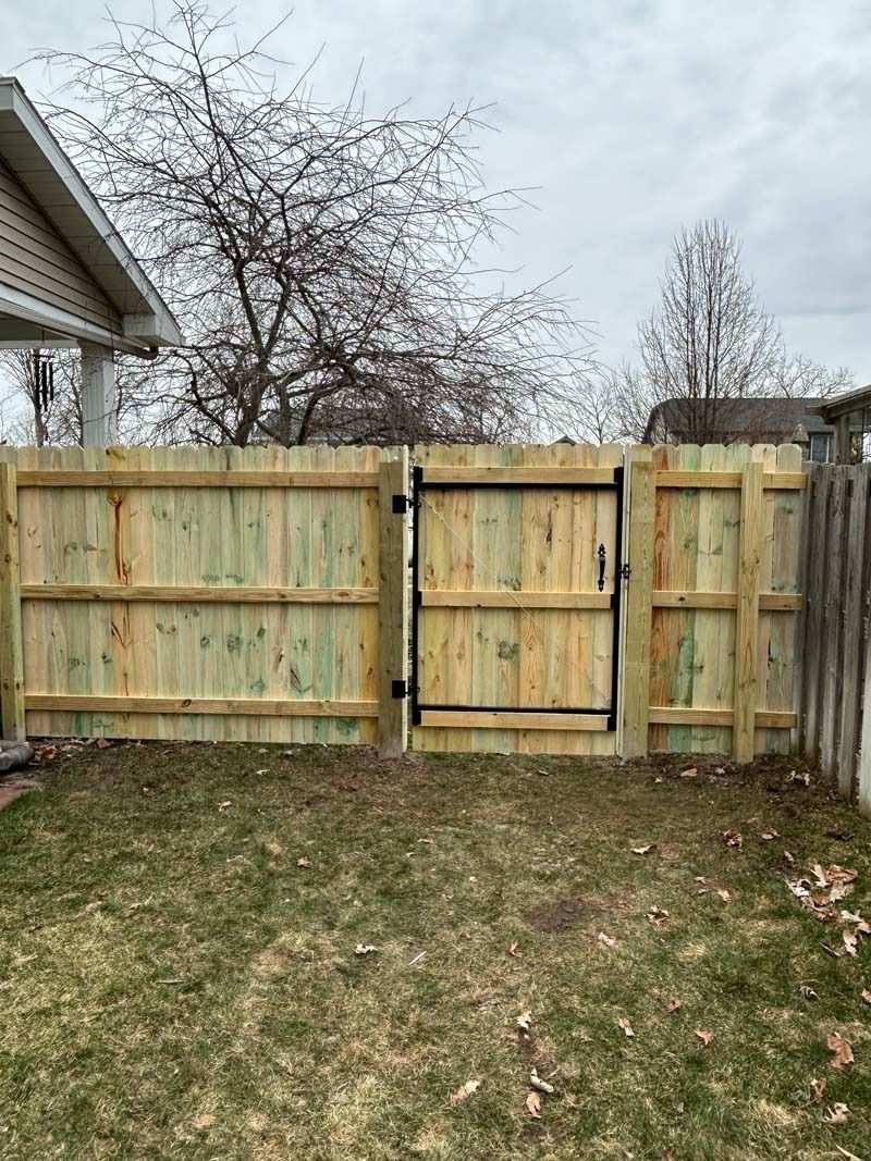 A wooden fence with a gate in a grassy yard, under a cloudy sky.