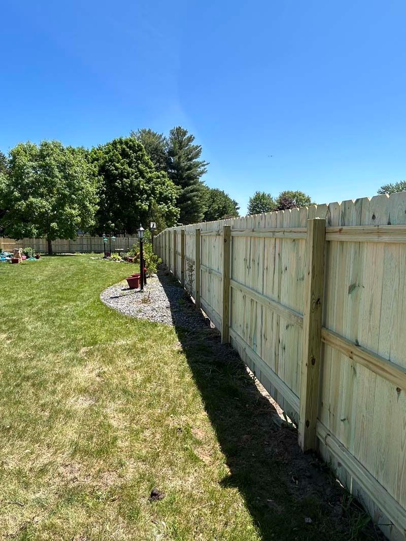 A newly built wooden fence along a green lawn under a bright blue sky.