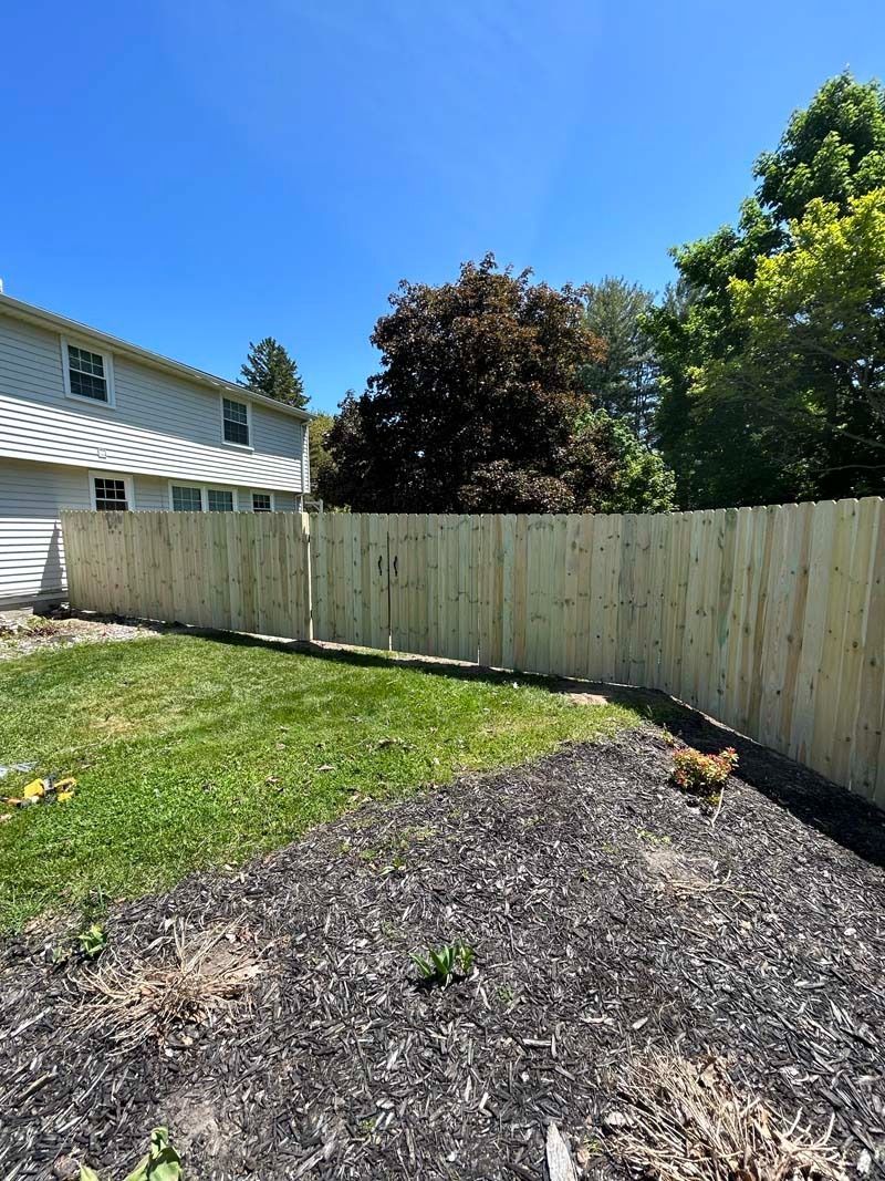 Backyard with a new wooden fence, green grass, and trees under a blue sky.