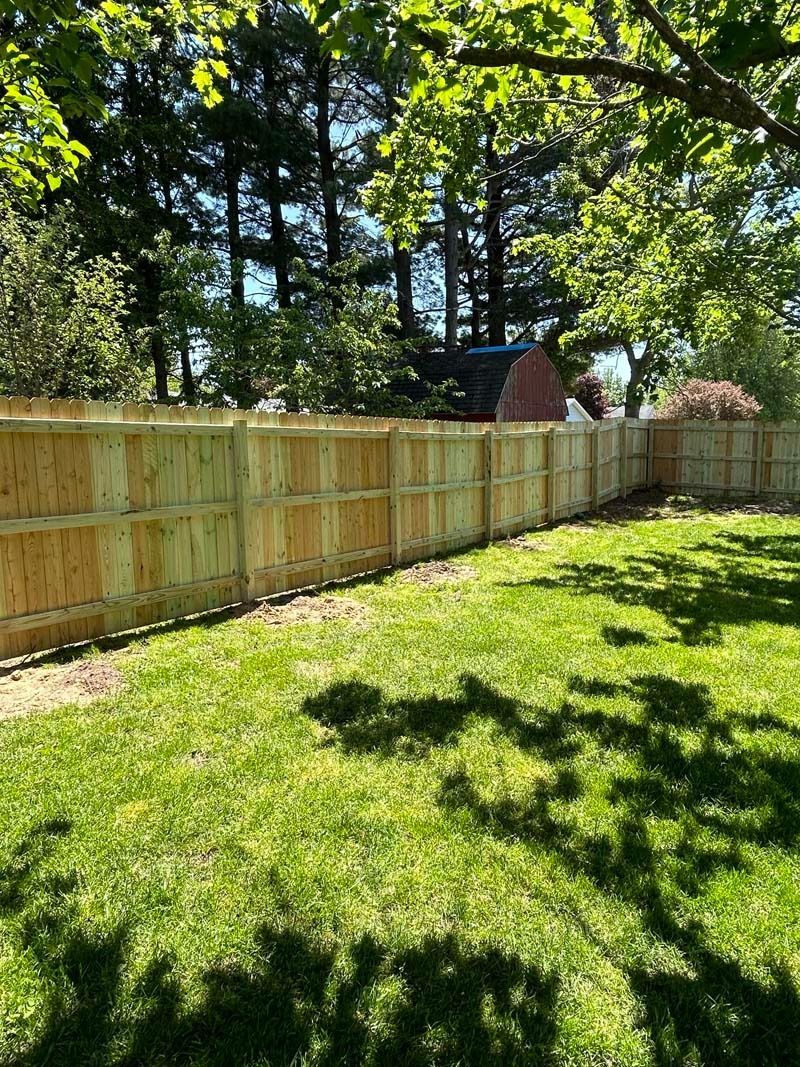 A new wooden fence bordering a grassy yard, trees in the background.