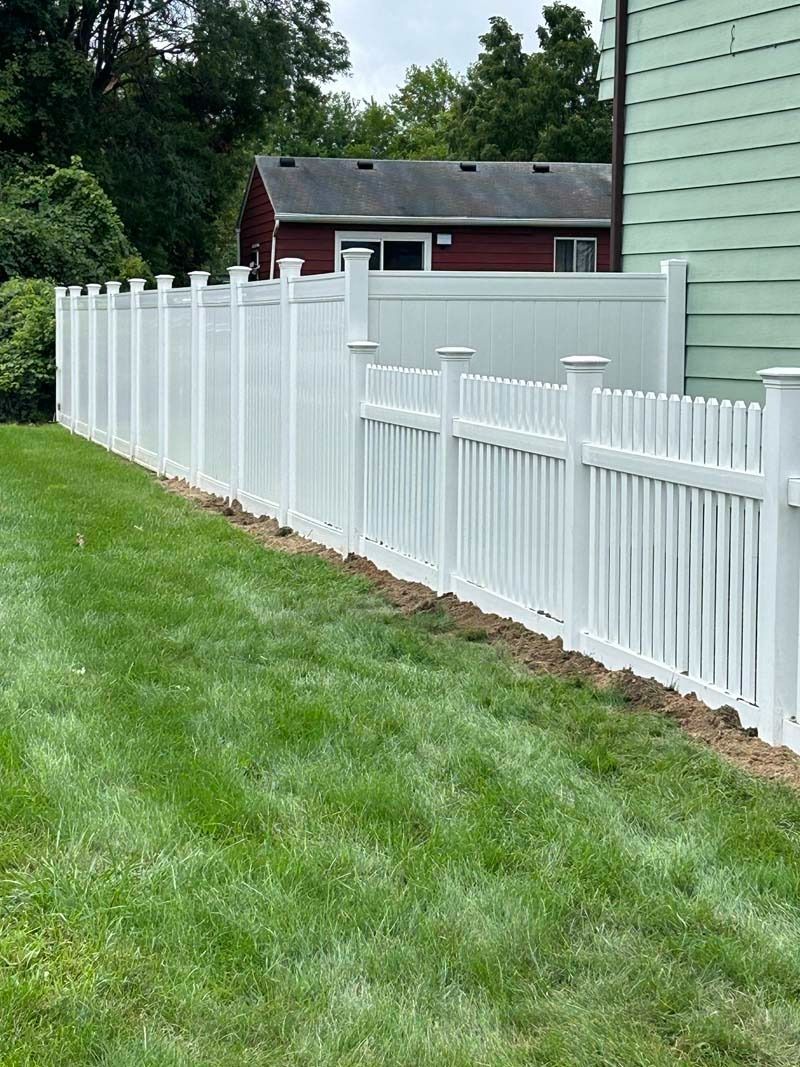 White vinyl fence along green grass in front of a house.