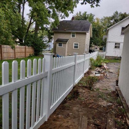 White picket fence in a backyard, with two houses visible in the background.
