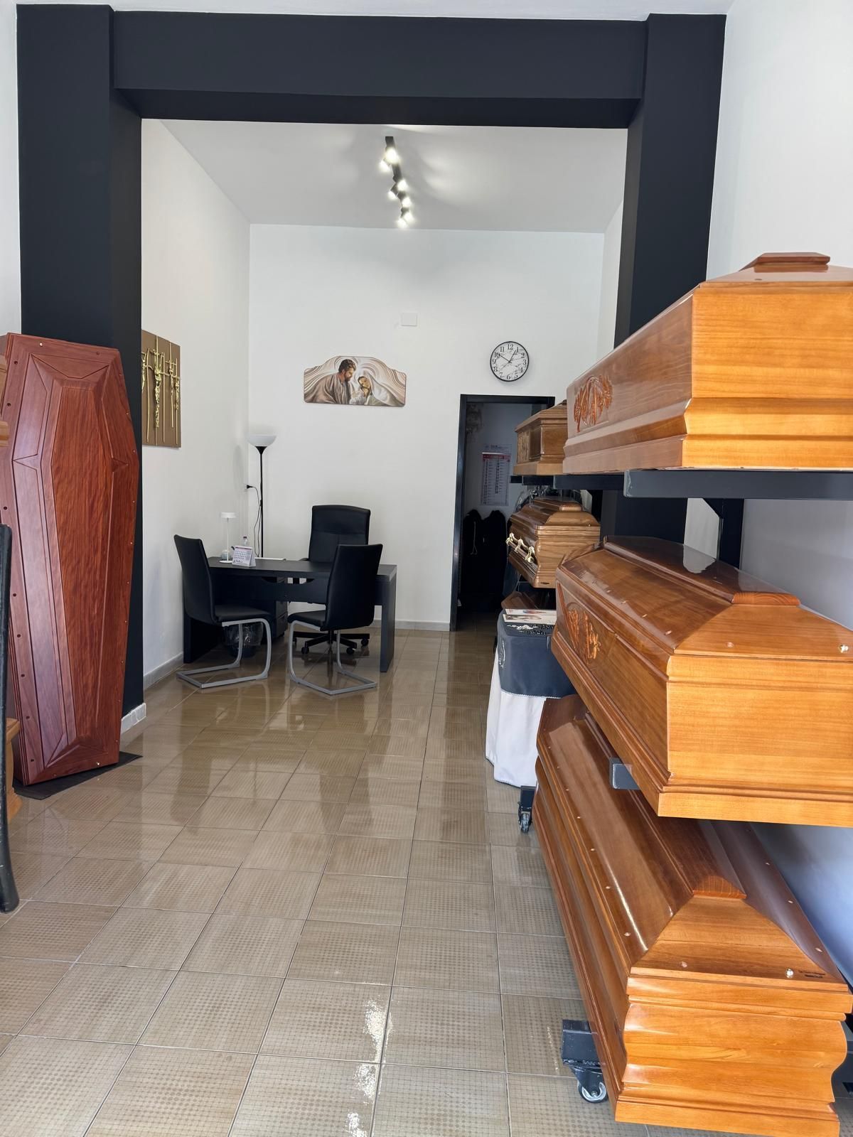 Interno di uno stretto caffè con sedie e un orologio a muro; scaffali in legno si trovano sul lato destro.