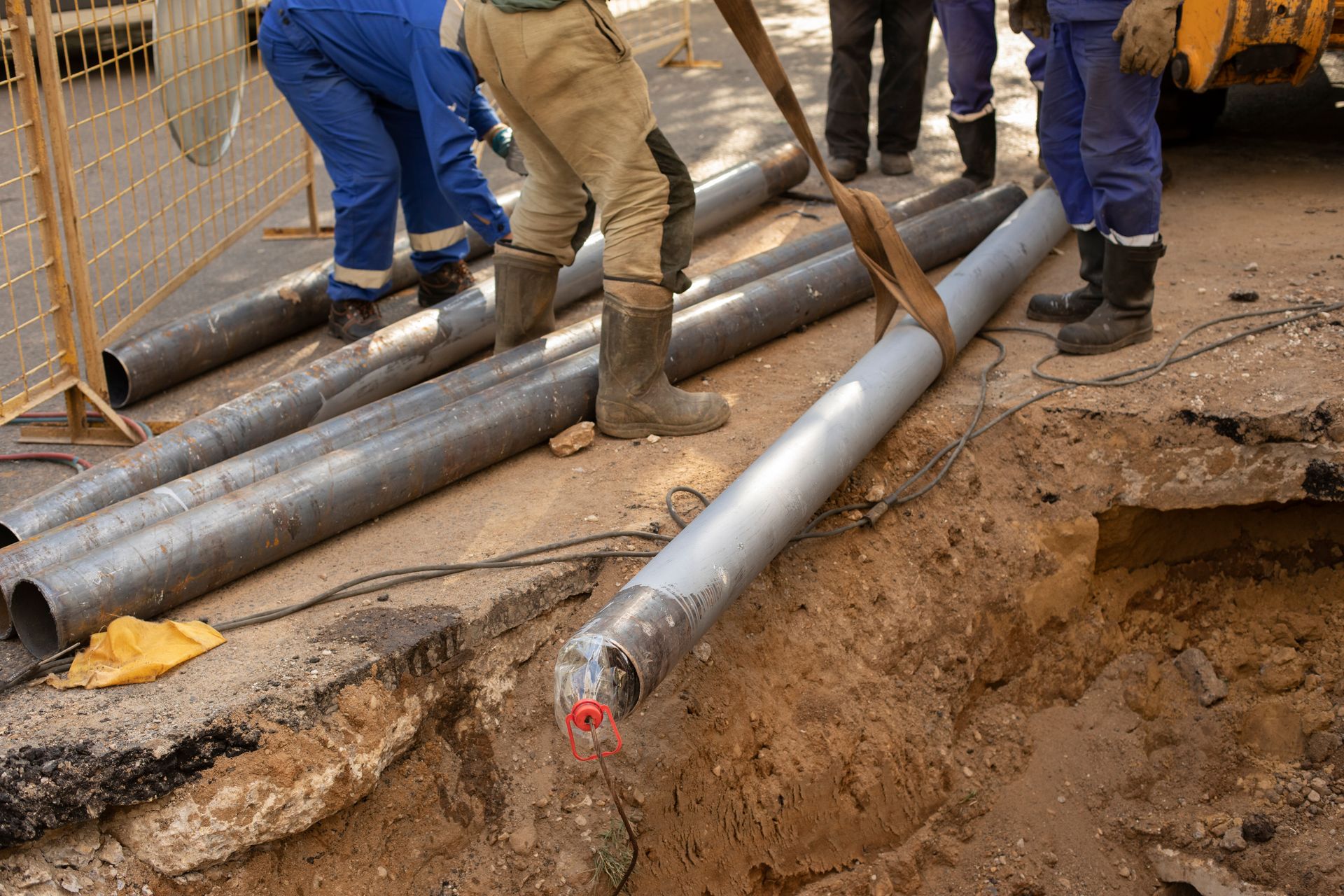 Construction workers positioning large steel pipes beside an excavation trench.