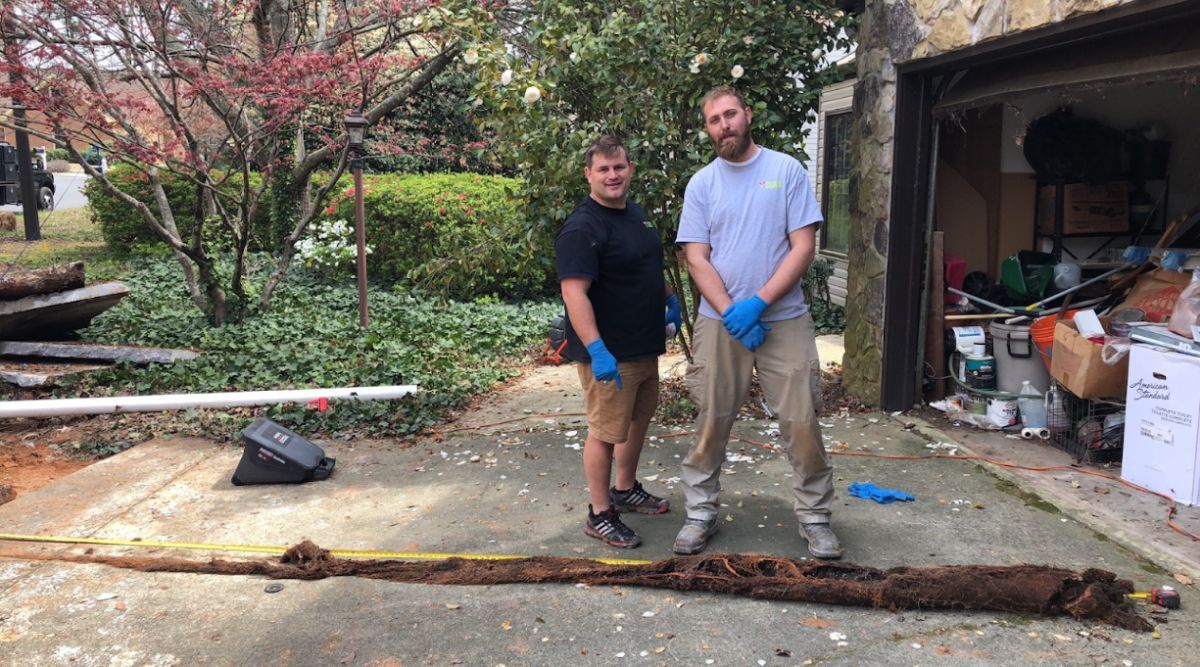 Two men are standing next to a large piece of dirt in front of a garage.
