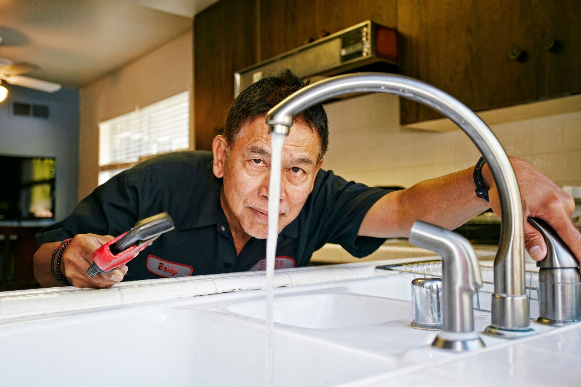 Plumber examining sink in kitchen.