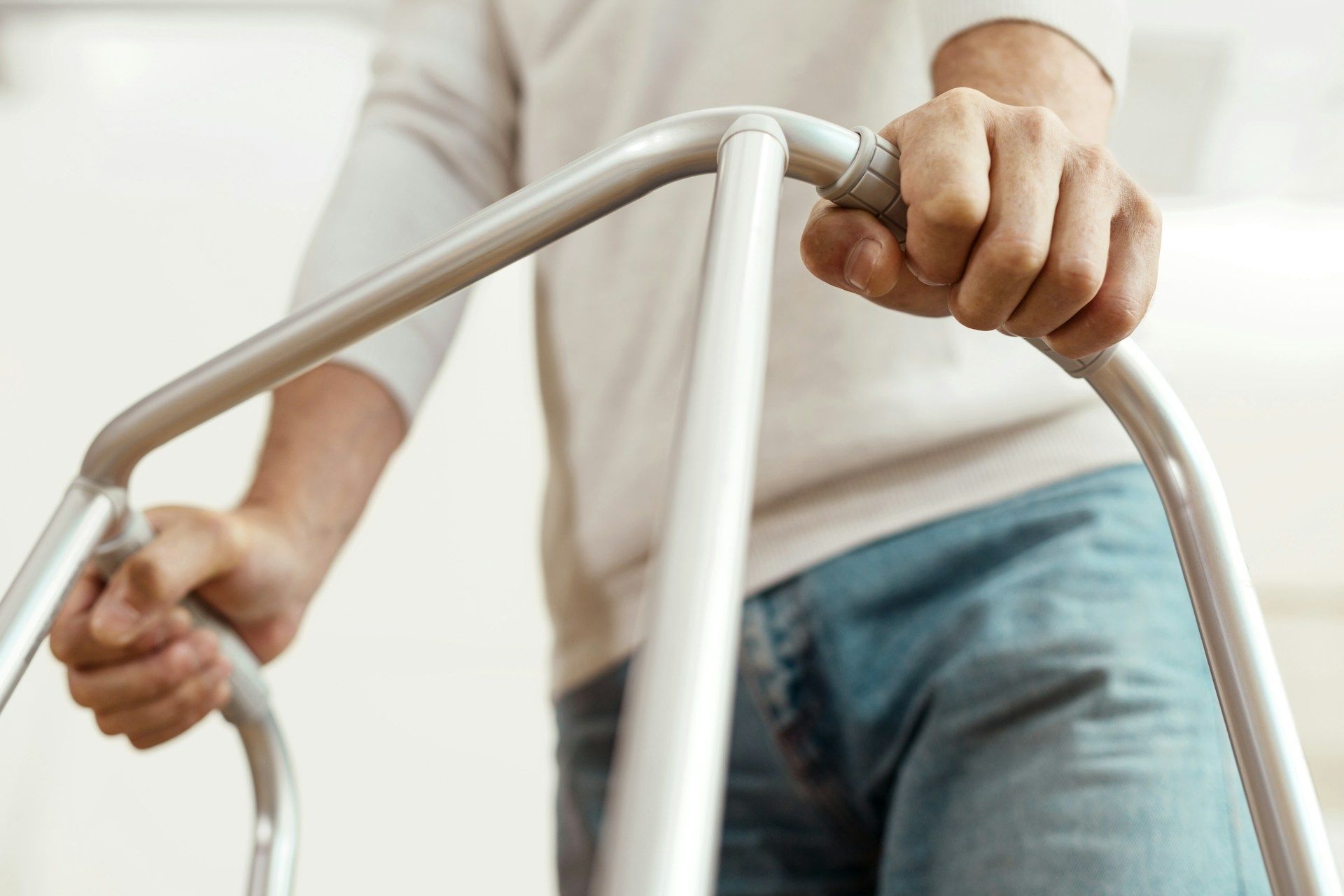 Person's hands holding a silver walker, wearing jeans and a white shirt.