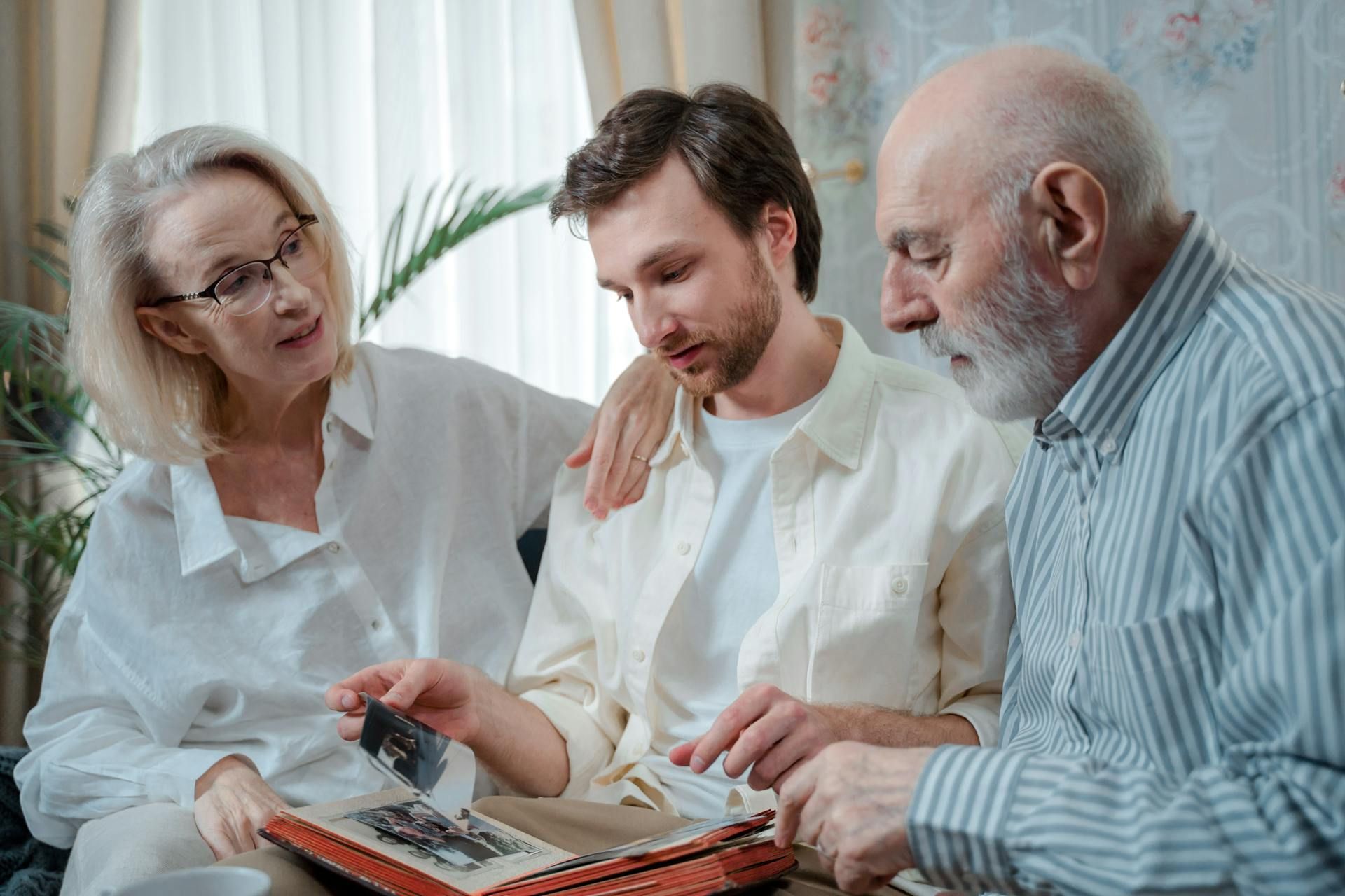 A family looking at a photo album together indoors. Woman and man on either side of the man in the middle.