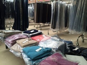Esposizione di un negozio di abbigliamento: maglioni impilati e confezionati in vari colori; scaffali di pantaloni sullo sfondo.