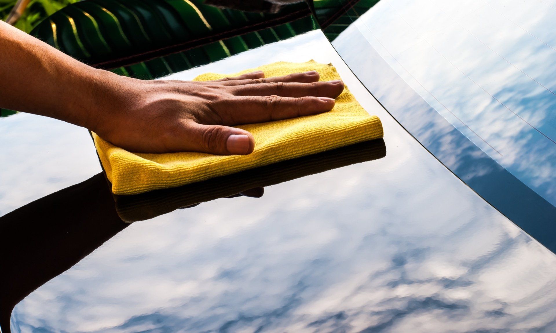 A person is cleaning a car with a yellow towel.