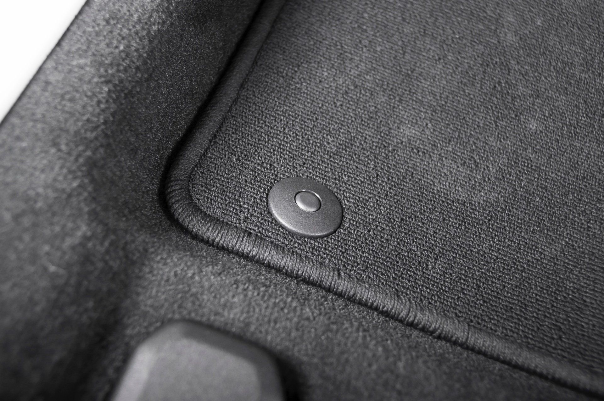 A close up of a black car mat with a button on it.