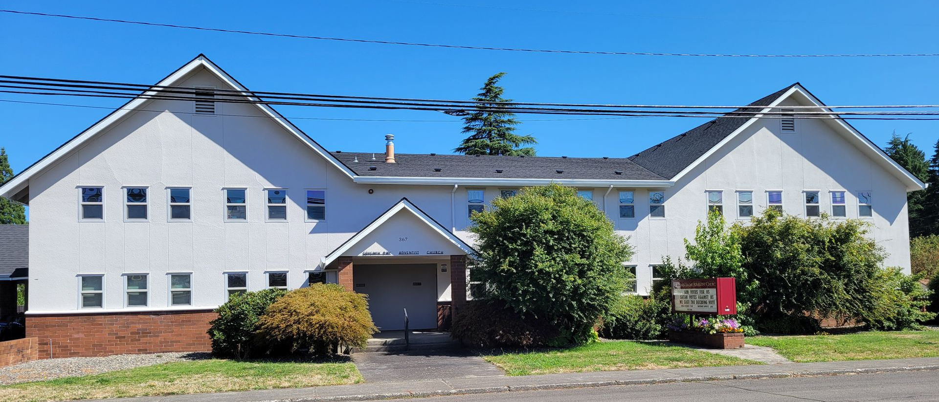 White two-story building with multiple windows, bushes in front, and a cloudy sky.