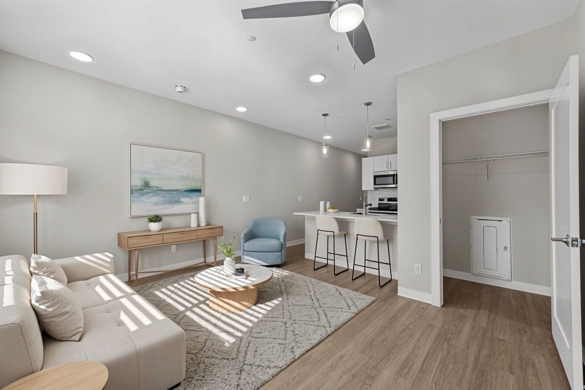 Modern apartment living room with light walls, hardwood floors, and a kitchen.