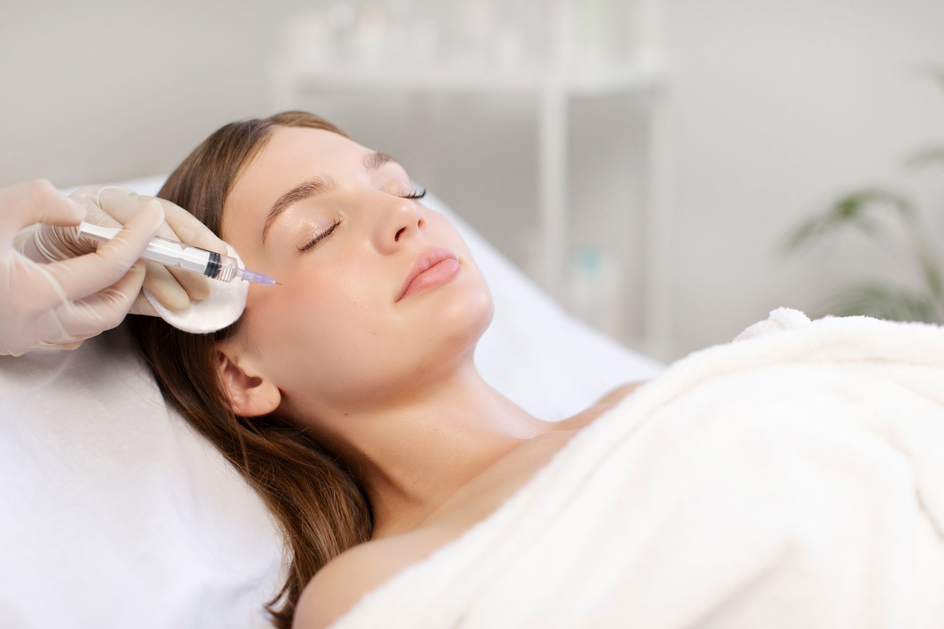 Woman receiving facial treatment with a handheld device while lying on a white spa bed