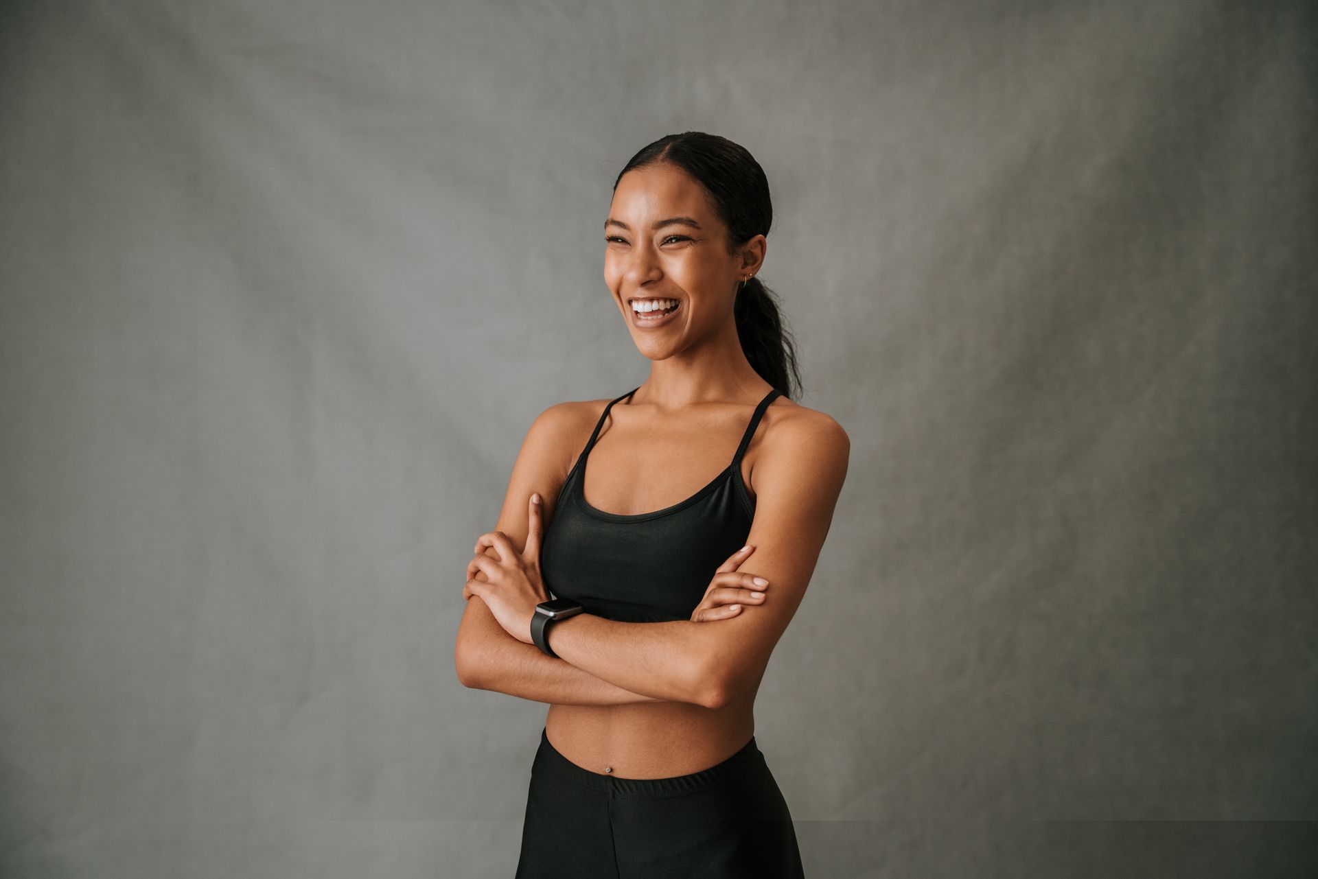 a woman with her arms crossed is smiling and wearing a smart watch