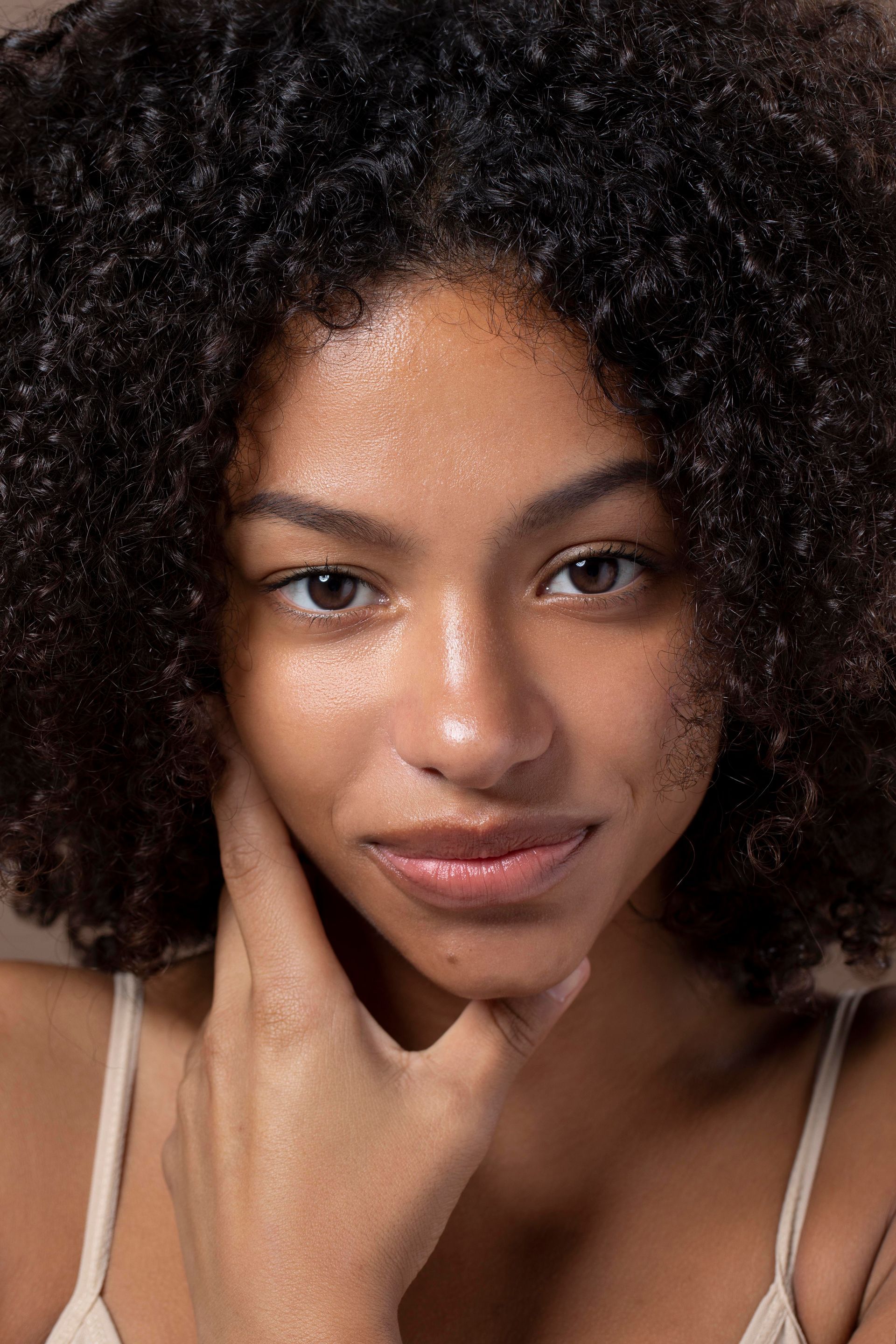 a woman with curly hair touches her face with her hand