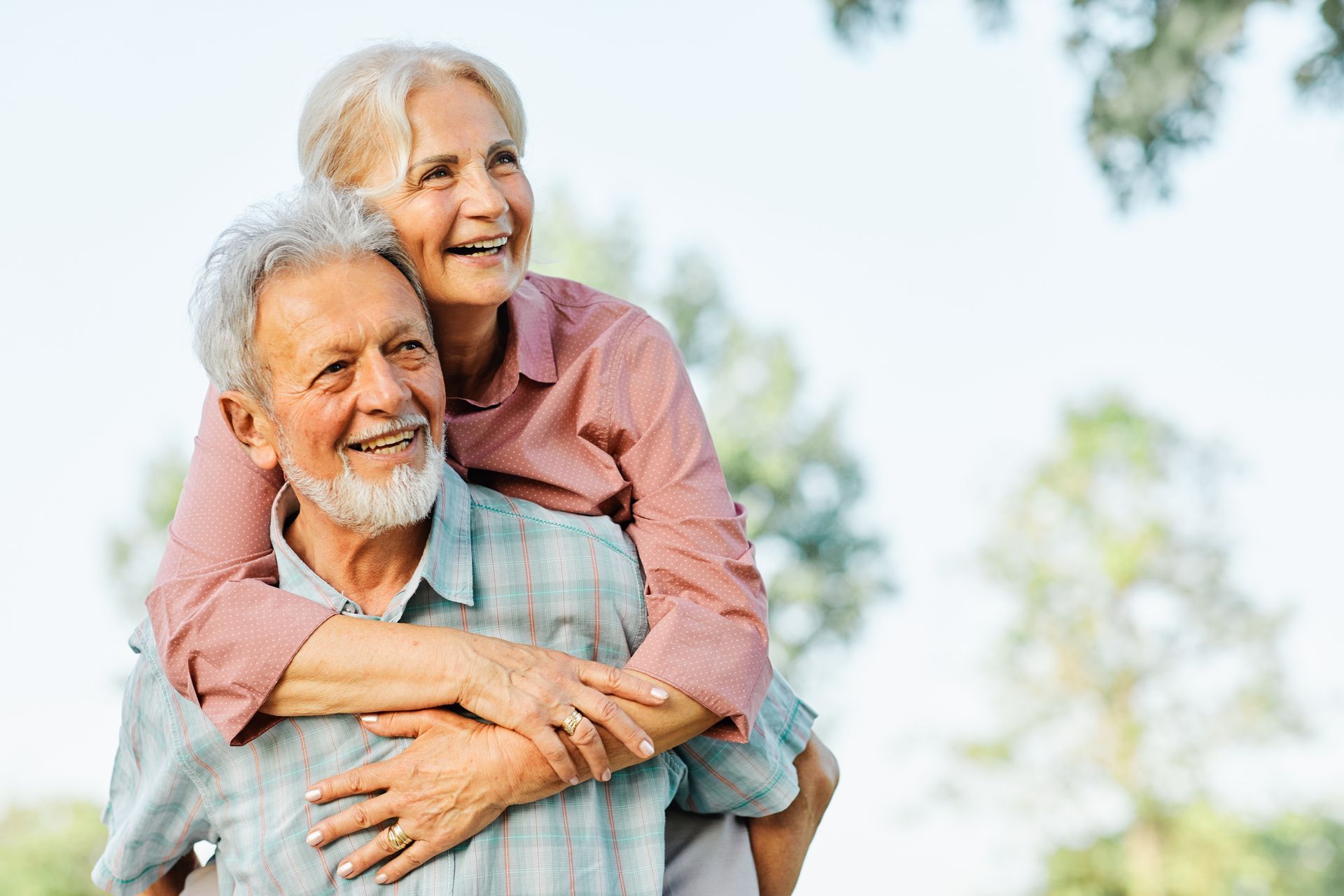 Smiling couple hugging outdoors in a bright park with blurred trees in the background