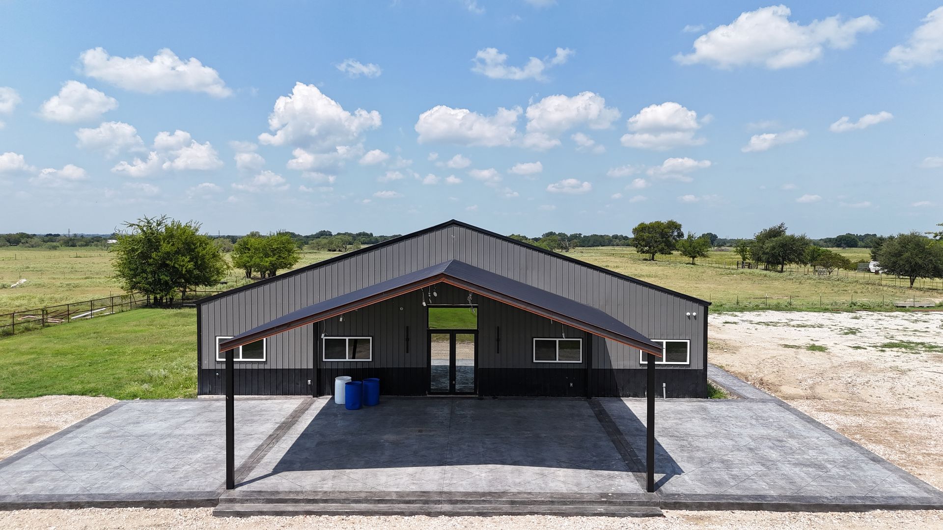 Small pavilion with a metal roof and covered porch, set in a grassy open field under a blue sky.