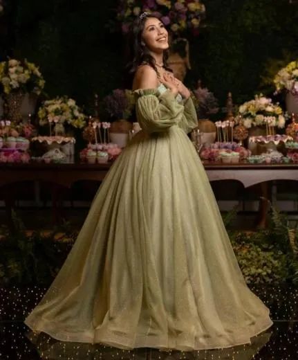 Woman in a flowing pale green gown posing in a flower-filled garden setting