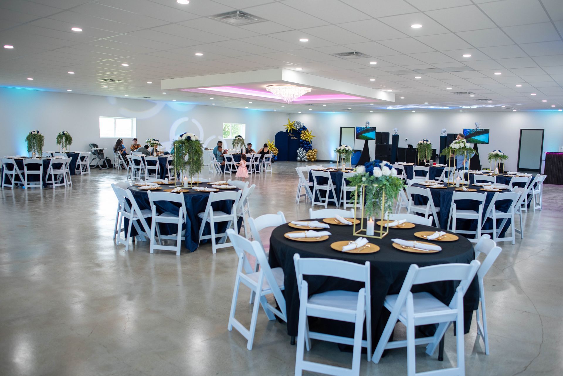 Large banquet hall with round tables, white chairs, and place settings under bright ceiling lights
