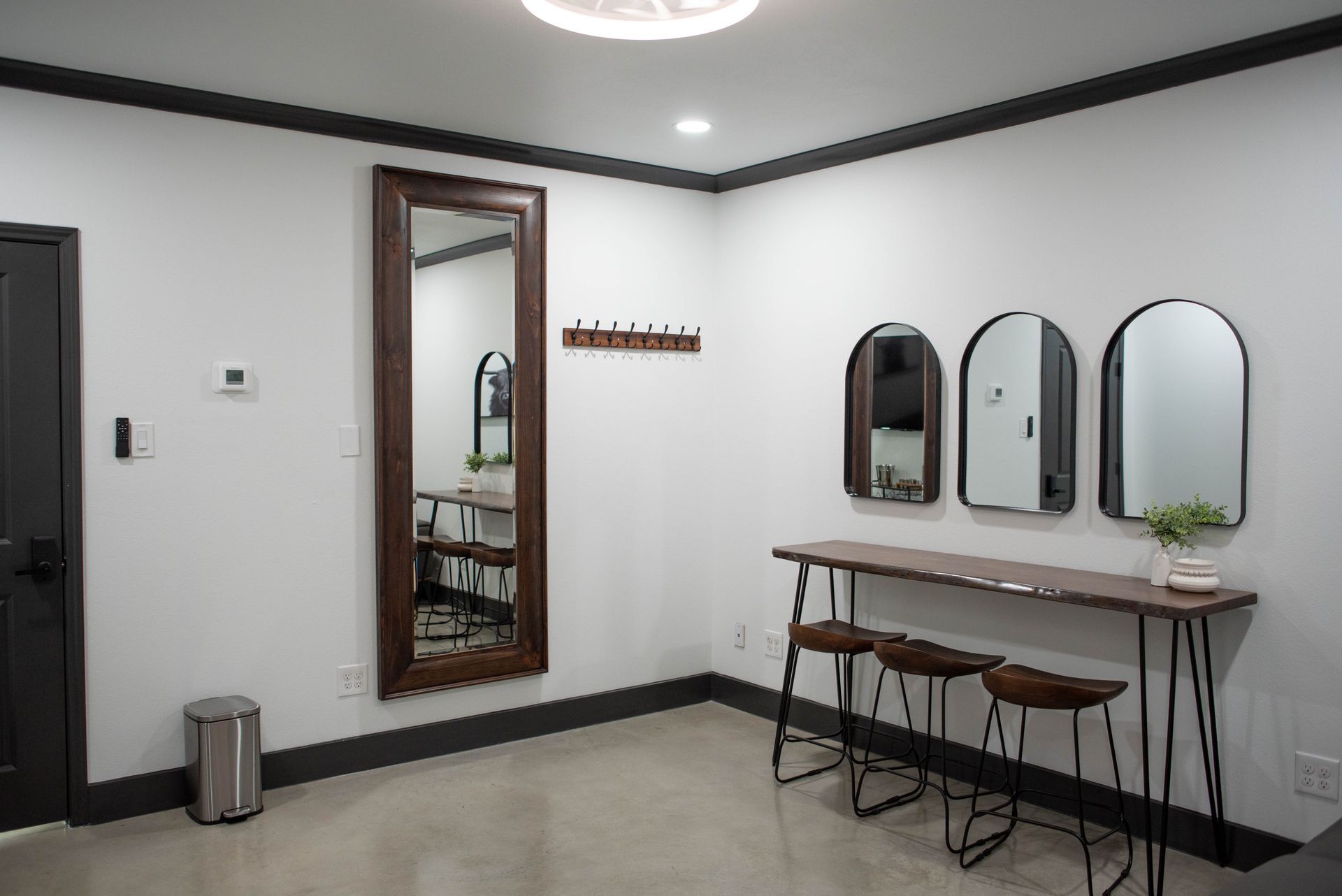 Minimalist room with wall mirrors, small desk, stools, and a trash can on white walls.