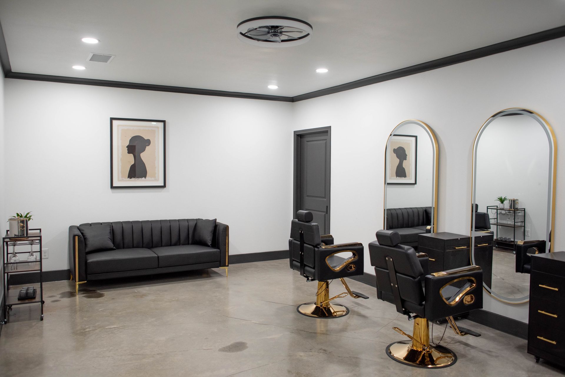 Modern hair salon interior with black styling chairs, mirrors, sofa, and framed wall art.