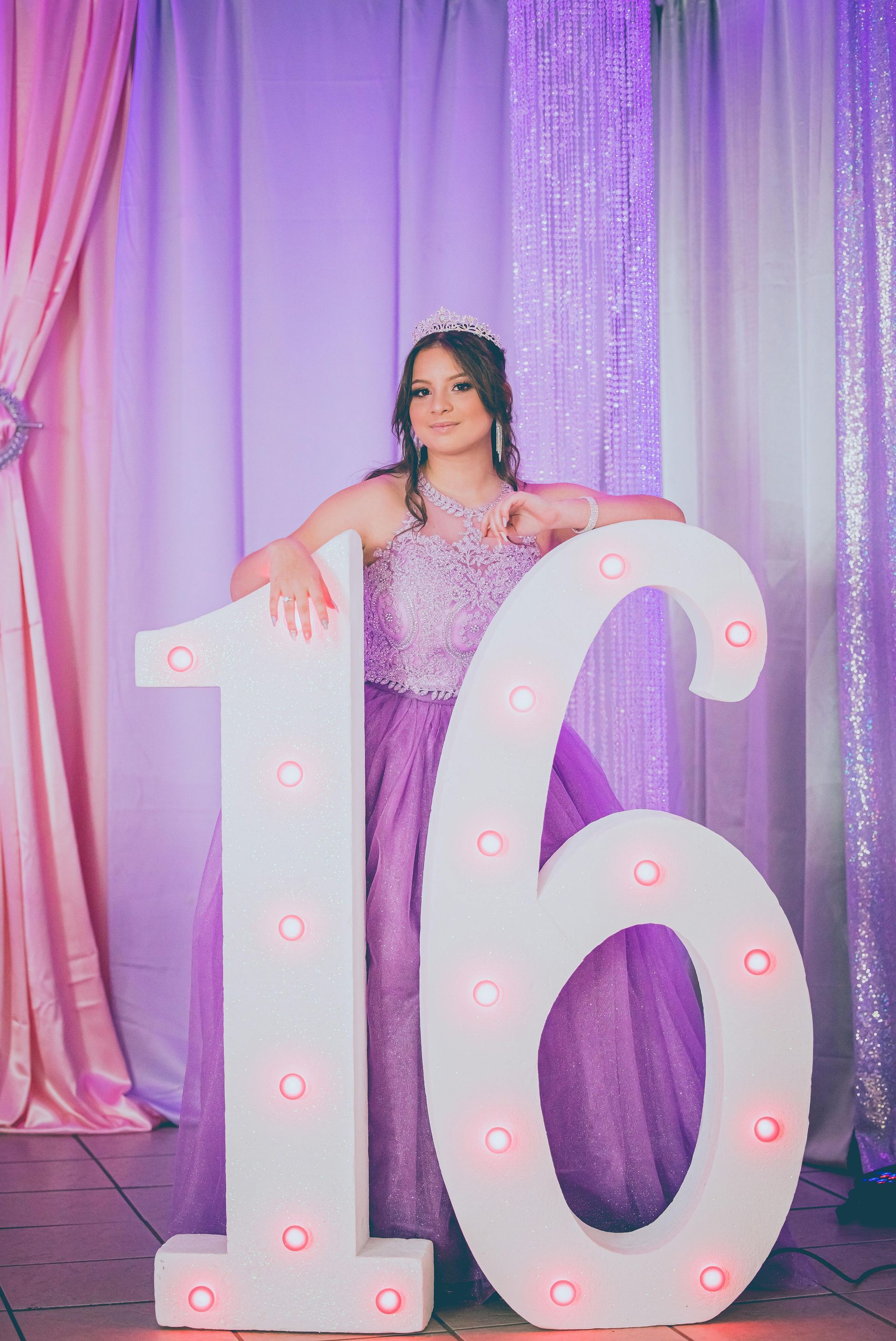 Teen posing behind large illuminated “16” numbers in a purple party backdrop