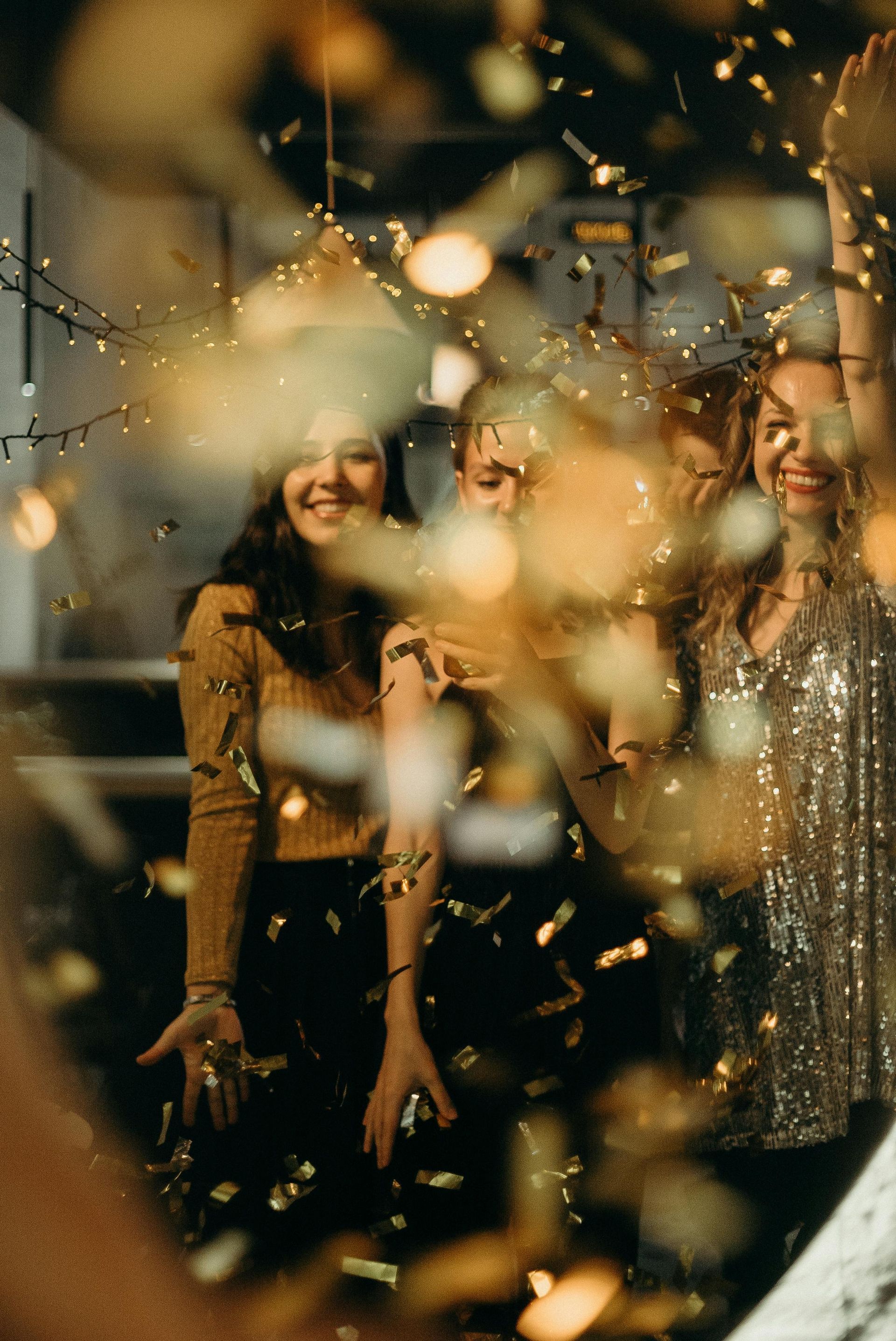 Two smiling people amid golden confetti lights, standing in a festive indoor scene.