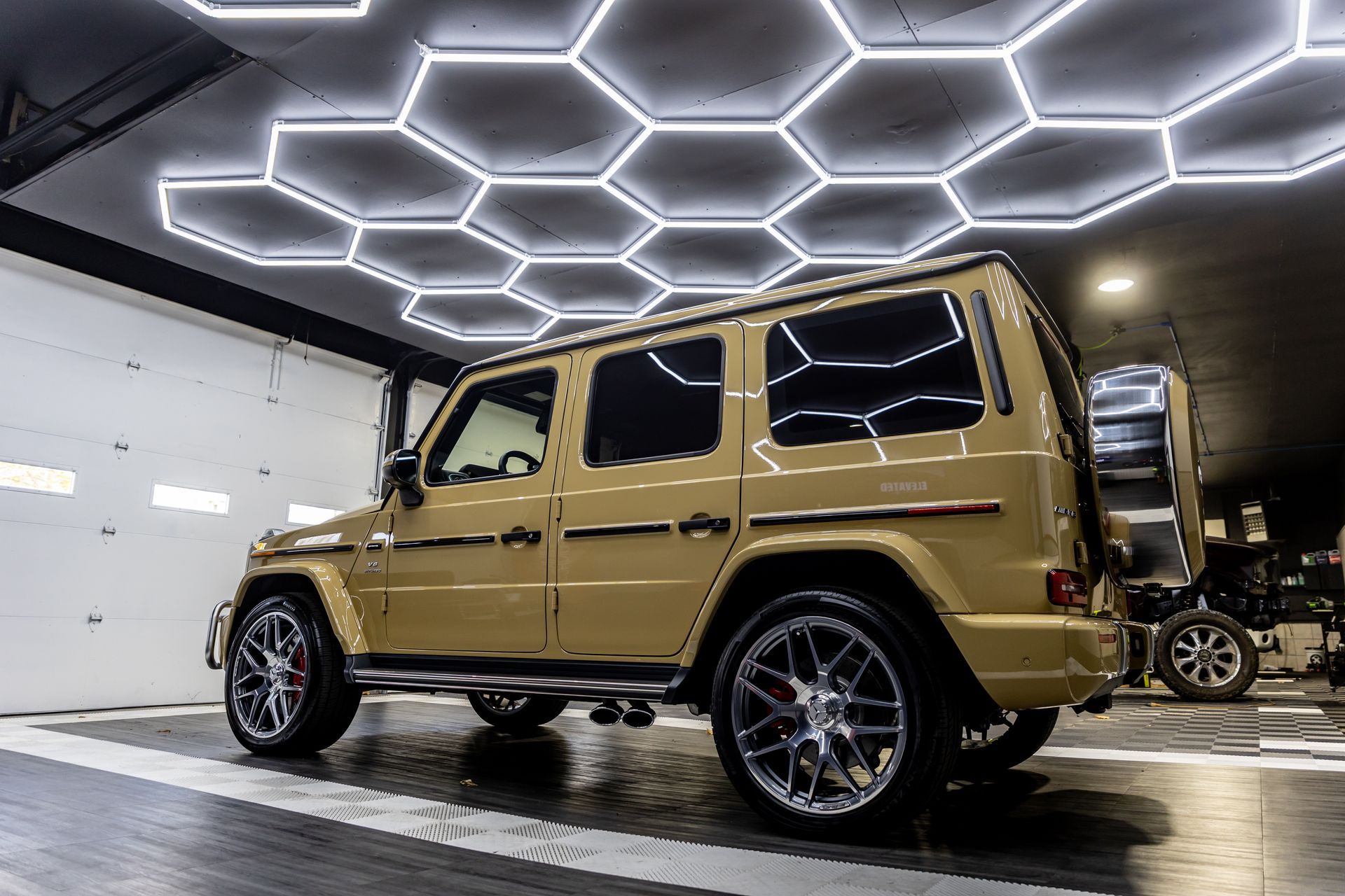 A mercedes benz g63 is parked in a garage under a honeycomb ceiling.