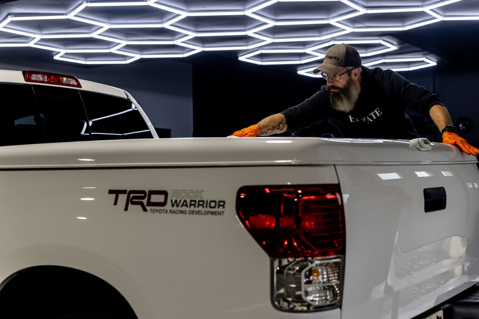 A man is cleaning the hood of a white truck in a garage.