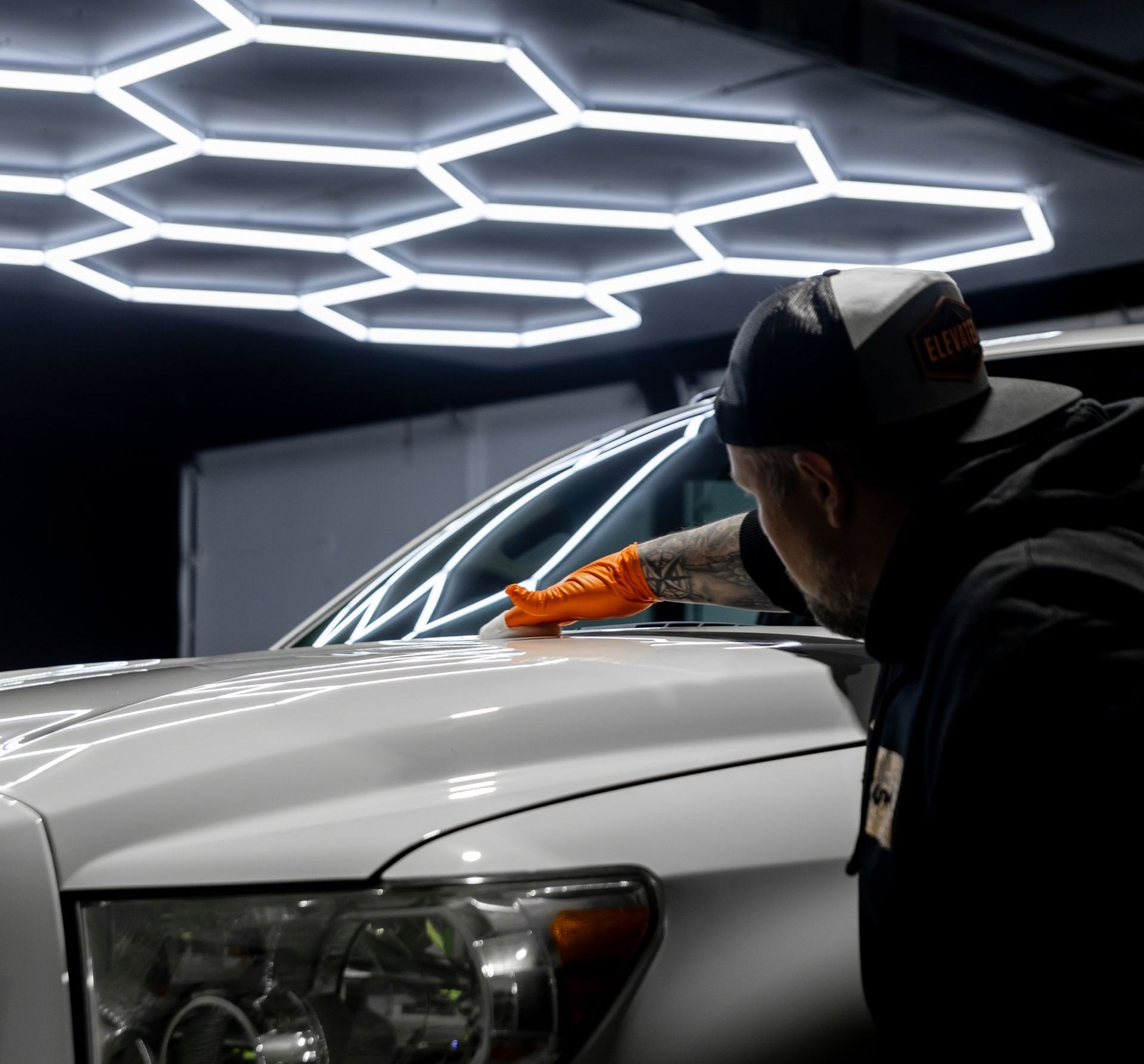 A man is cleaning the hood of a white truck in a garage.