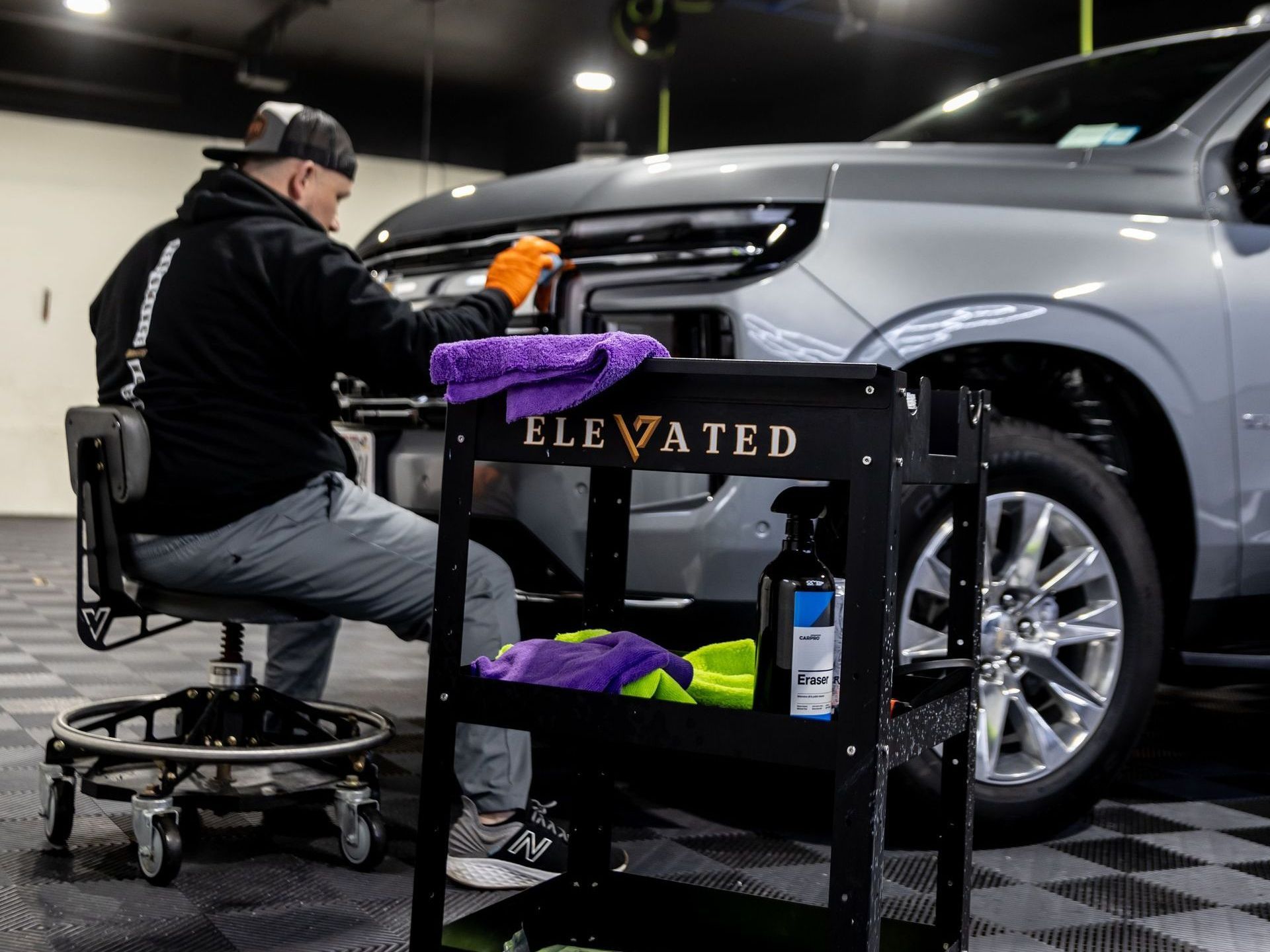 A man is sitting on a stool working on a car in a garage.
