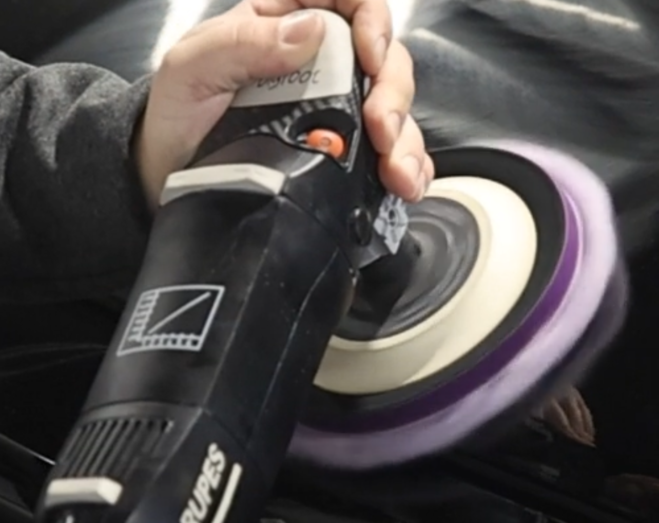 A man is polishing a car with a machine.