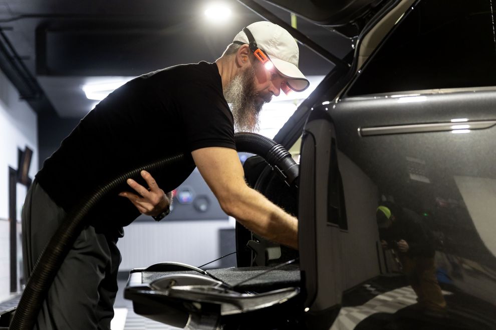 A person is polishing the tail light of a car with a machine.