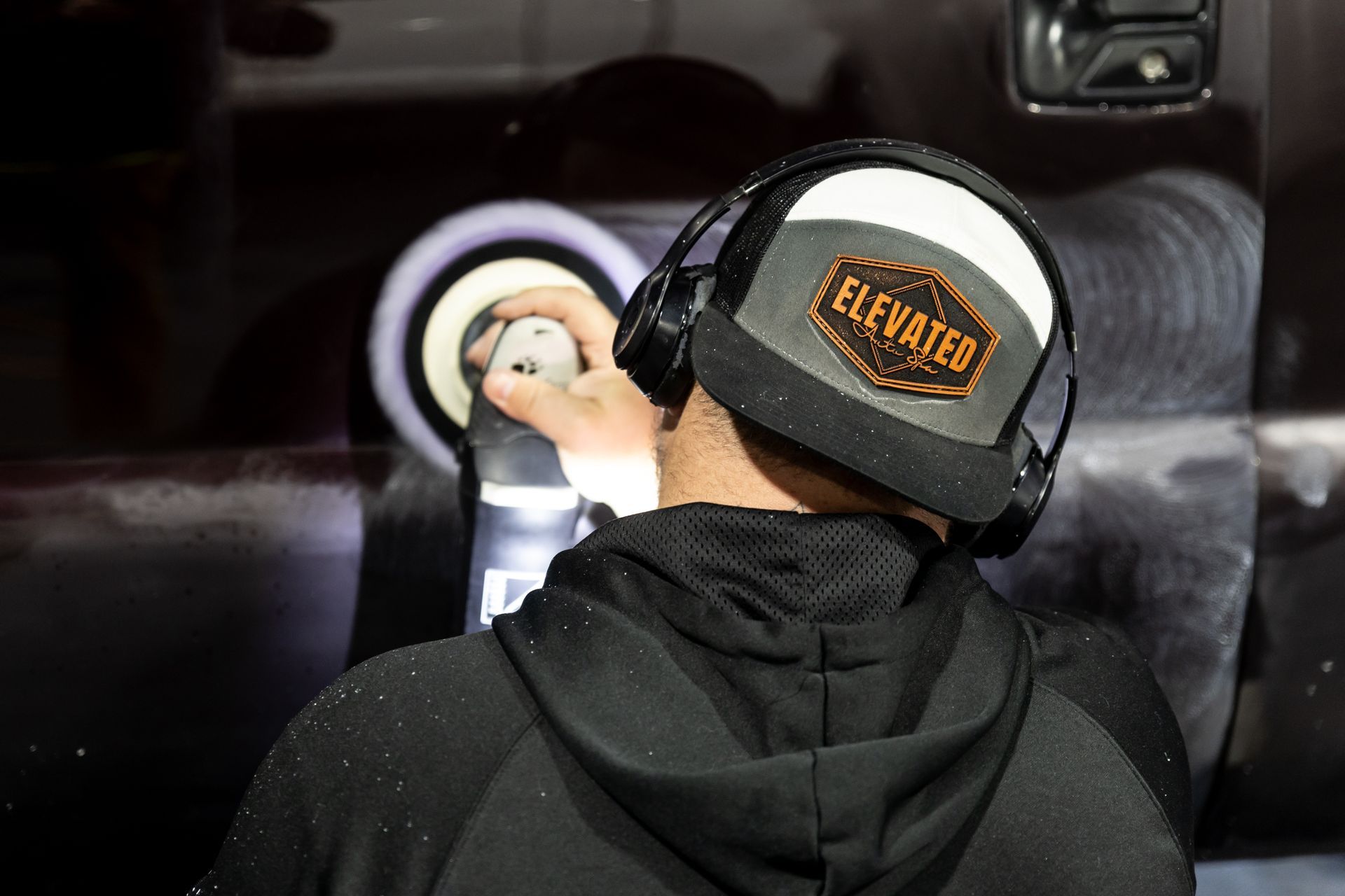 A man wearing headphones is polishing a car.