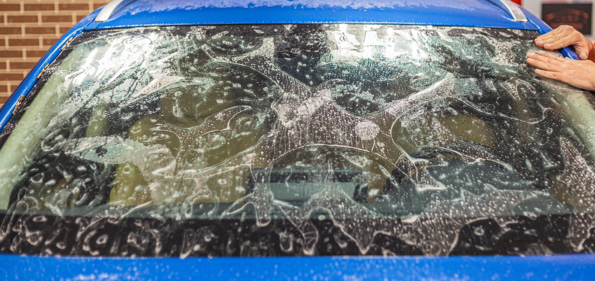 A man is applying tinted glass to the windshield of a car.