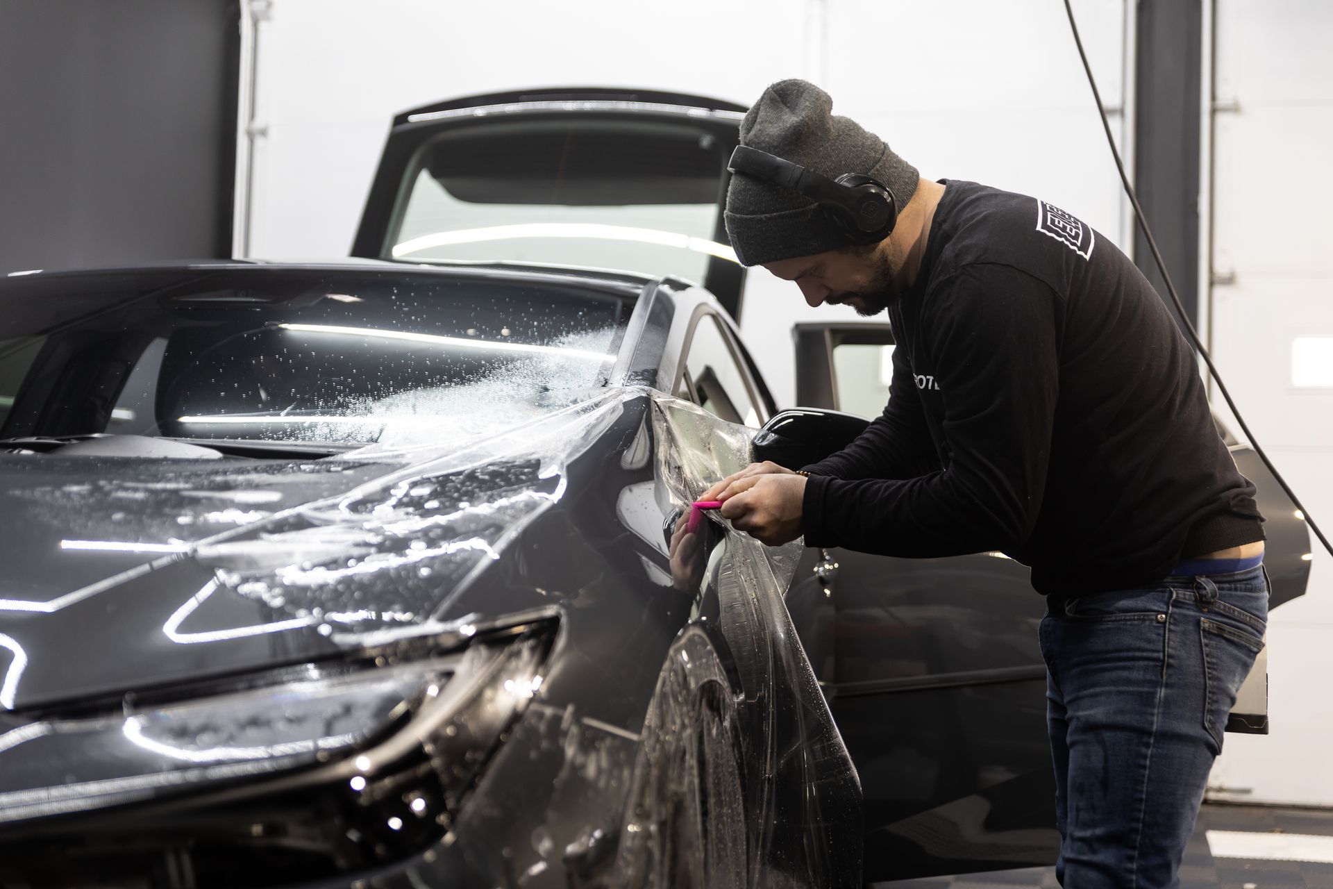 A person is applying protective film to a car with a blue spatula.