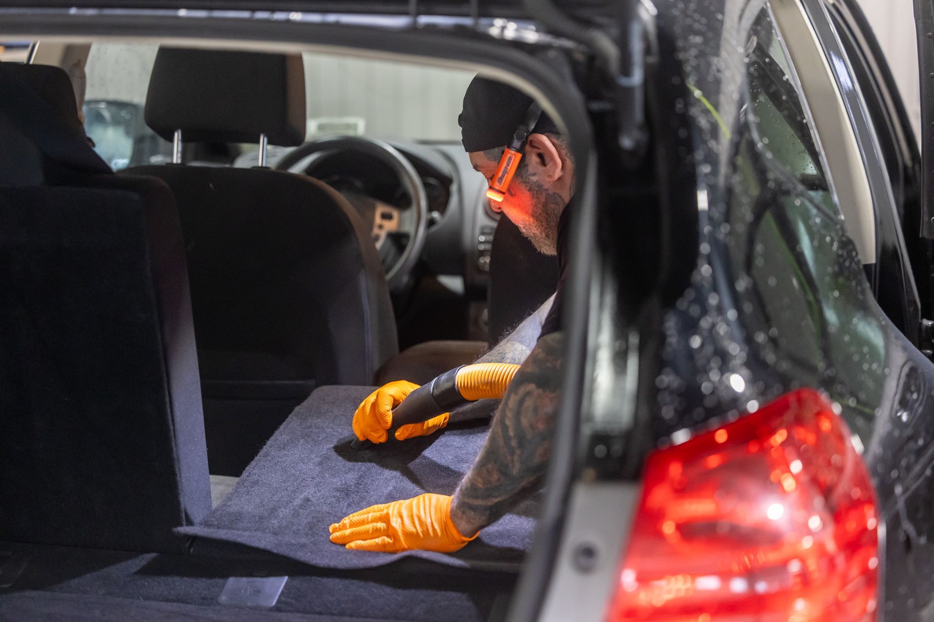 A man is cleaning the trunk of a car with a vacuum cleaner